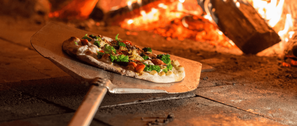 A roasted vegetable pizza being taken out of a Bertucci's brick oven