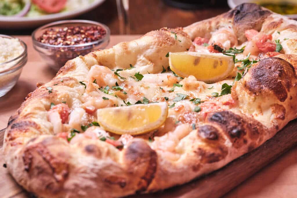 Bertucci's Artisan Hand-Stretched Shrimp Scampi Pizza with side of crushed red peppers and parmesan cheese