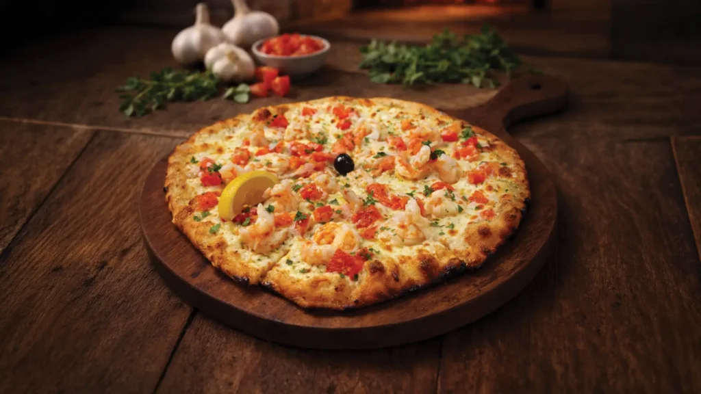 Shrimp Bella Venezia pizza topped with tender shrimp, diced tomatoes, fresh herbs, and melted mozzarella on a wood-fired crust, served on a wooden board.
