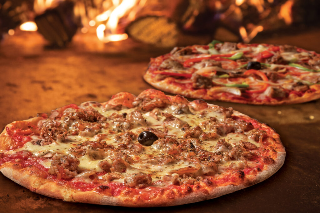 Two pizzas inside a brick fire oven